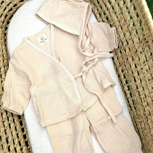 Beige baby outfit with a hat on a white surface with a wicker basket background