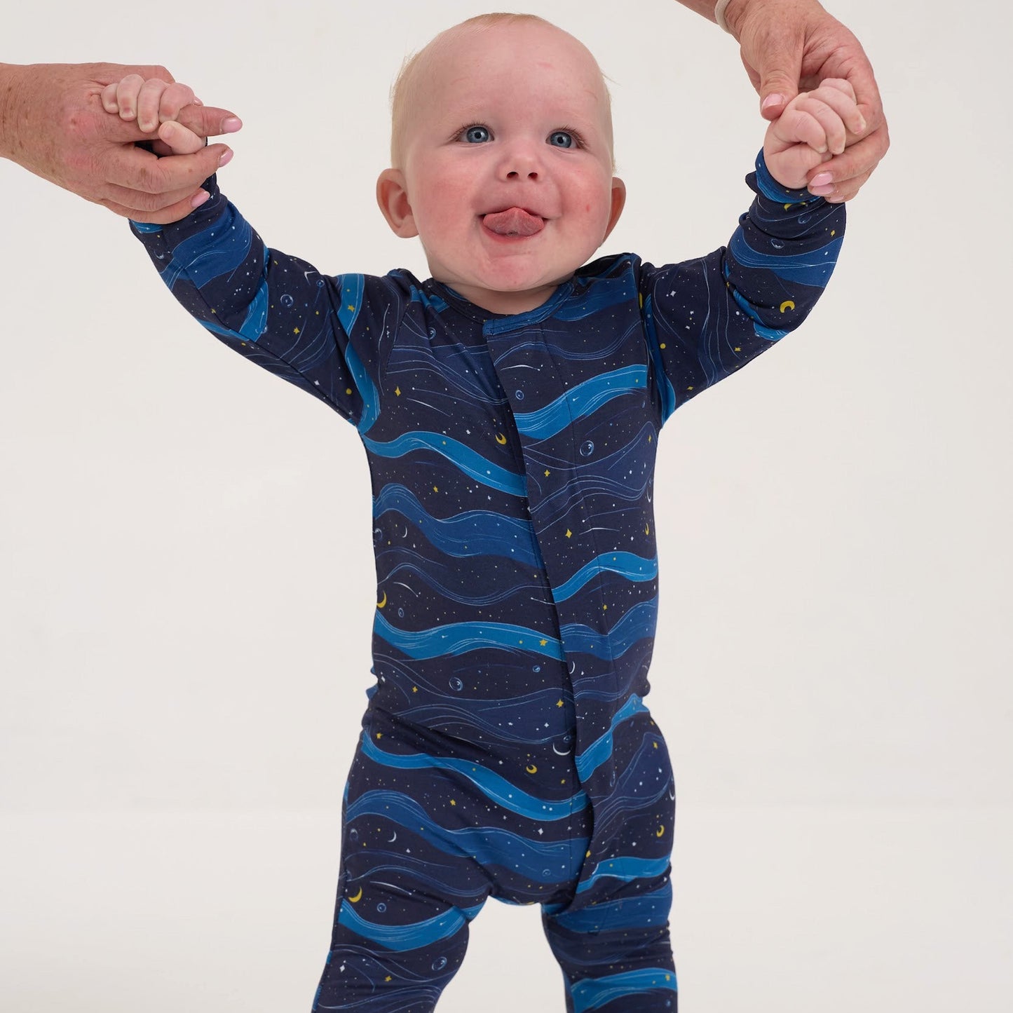 Baby wearing a blue wave-patterned onesie standing on a white background
