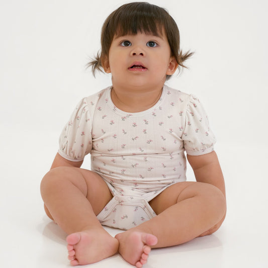 Baby wearing a white onesie with small patterns on a white background