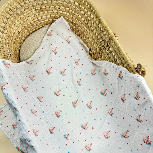 Baby blanket with sailboat pattern draped over a wicker basket on a beige background 