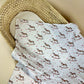Muslin blanket with rocking horse pattern draped over a wicker basket on a beige background